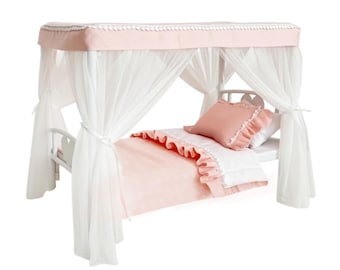 Puede incluir: Una cama de muñeca blanca con estructura de dosel que presenta una cubierta de tela rosa suave con ribete de pompones blancos. Incluye cortinas blancas transparentes, una almohada rosa con volantes, una almohada blanca y una manta rosa.