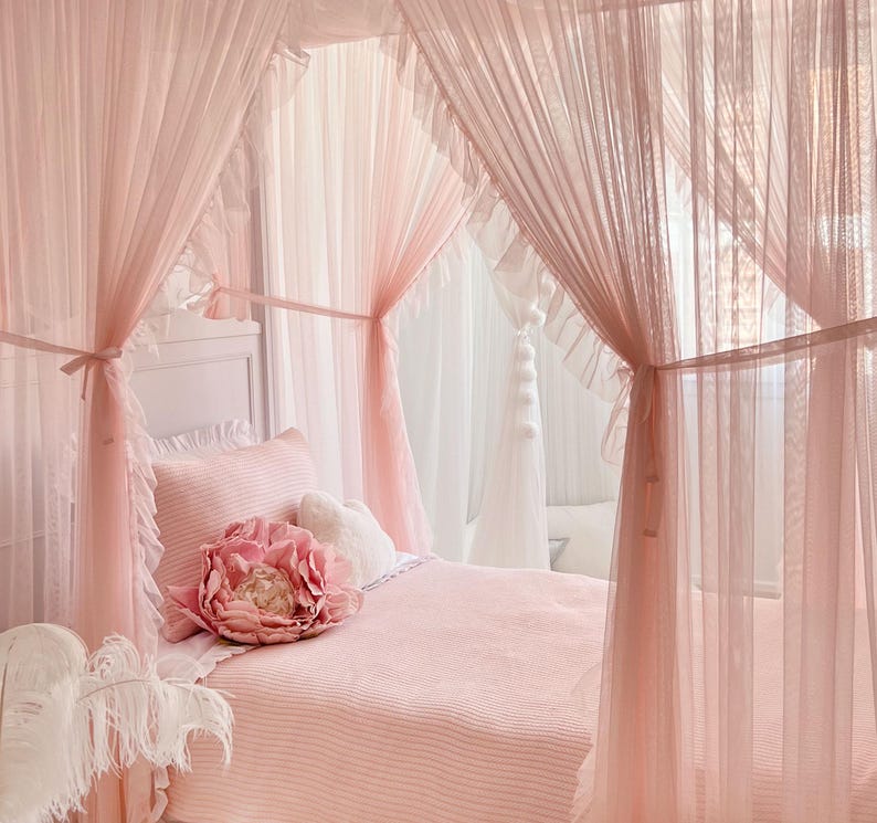 May include: A pink canopy bed with a white headboard and a pink and white striped comforter. A large pink flower pillow is on the bed. The canopy is made of sheer pink fabric with ruffles.