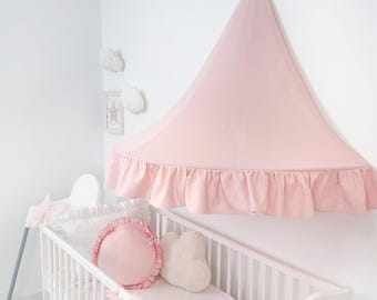 May include: A baby's nursery with a white crib and pink canopy. The canopy is mounted on the wall and has a ruffled edge. The crib is decorated with pink pillows and a blanket. Decorative cloud-shaped wall hangings are also visible.