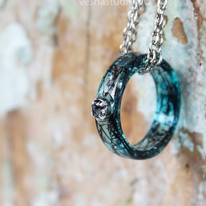 May include: A silver chain necklace with a turquoise ring pendant. The ring has a black and white design and a small silver stone in the center.