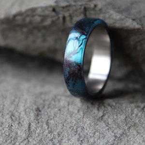 May include: A silver ring with a blue and black resin inlay. The resin has a swirling pattern.