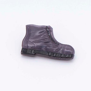 May include: A small, purple boot-shaped object with a textured surface. The boot has a lace-up design and a black sole. The object is likely a decorative item or charm.