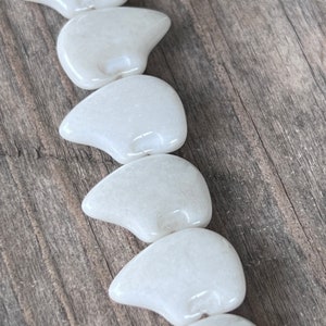 May include: A string of white ceramic beads shaped like polar bears. The beads are glossy and have a slightly textured surface.