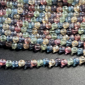May include: A strand of multi-colored glass beads with a ribbed texture. The beads are translucent and have a variety of colors, including blue, green, pink, and yellow.
