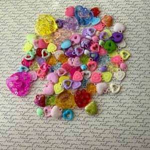 May include: Assortment of colorful plastic heart-shaped charms with a variety of textures and designs. The charms have a hole at the top for stringing or attaching to jewelry.