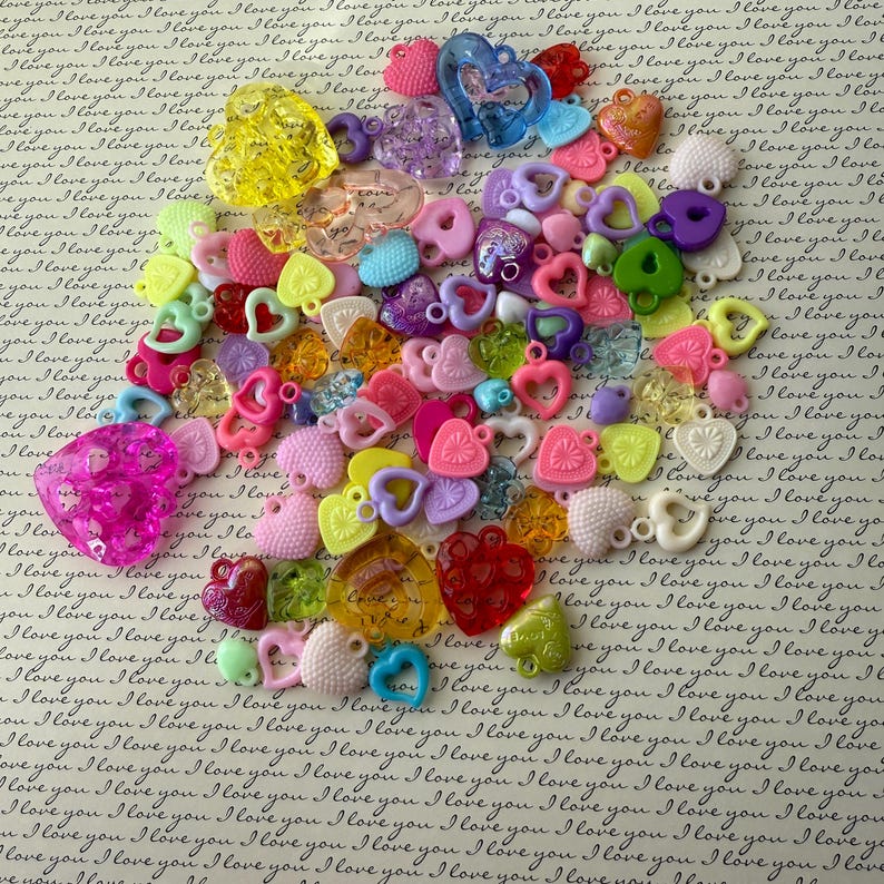 May include: Assortment of colorful plastic heart-shaped charms with a variety of textures and designs. The charms have a hole at the top for stringing or attaching to jewelry.