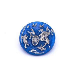 May include: A blue glass button with a silver design of a chariot pulled by two horses. The button has a raised design and a smooth, glossy finish.