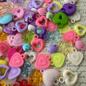 May include: Assortment of colorful plastic heart-shaped charms with a variety of textures and designs. The charms have a hole at the top for attaching to jewelry or other crafts.