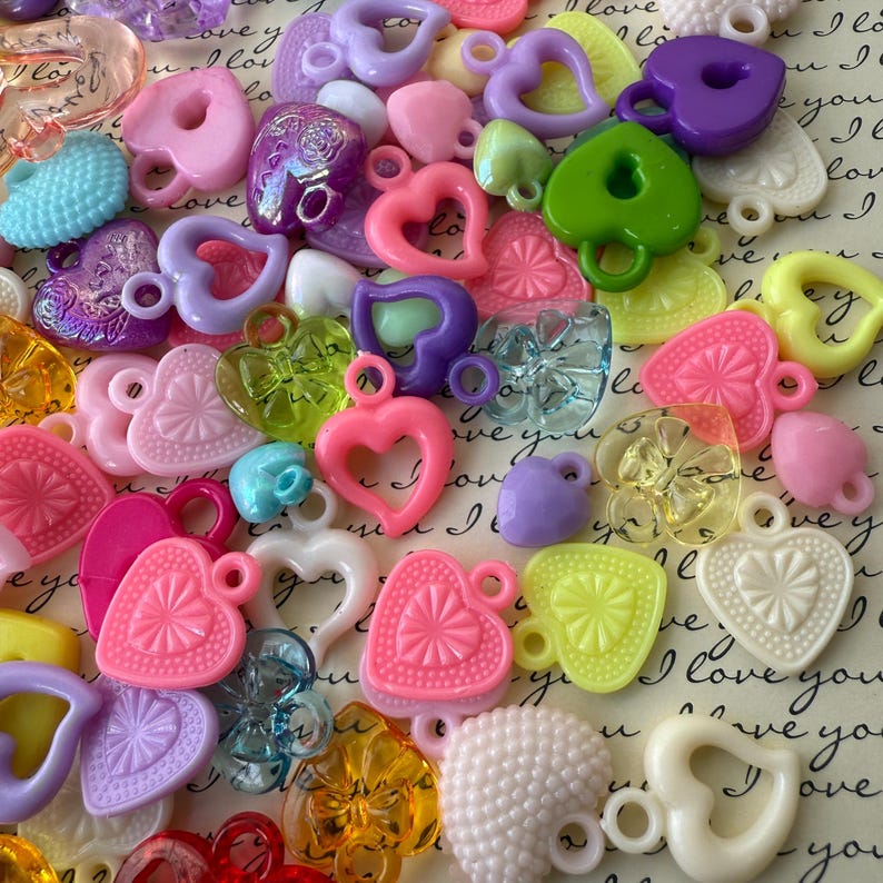 May include: Assortment of colorful plastic heart-shaped charms with a variety of textures and designs. The charms have a hole at the top for attaching to jewelry or other crafts.