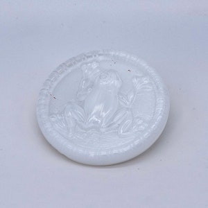 May include: White ceramic button with a raised design of a frog sitting on a lily pad.