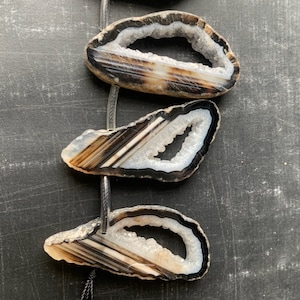 May include: Three agate slices with a white, translucent center and black and brown banding. The slices are strung on a black cord.