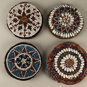 Könnte beinhalten: Vier runde, perlenbesetzte, dekorative Ornamente mit komplizierten Mustern in Rot-, Blau-, Weiß- und Brauntönen. Die Ornamente sind aus kleinen Perlen und Muscheln gefertigt.