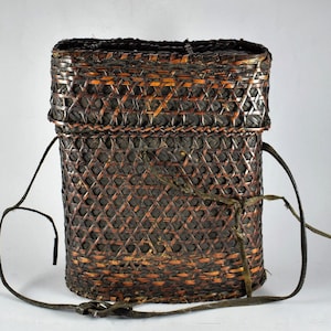 以下が含まれることがあります： 革のストラップが付いた、茶色と黒の籐で編まれたバスケット。バスケットは自然素材で作られており、素朴な外観をしています。