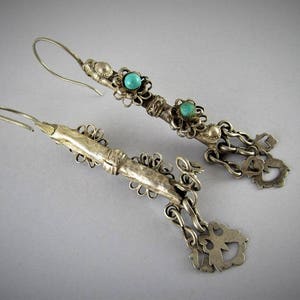 May include: A pair of silver earrings with turquoise stones and intricate filigree designs. The earrings are dangling and have a hook closure.