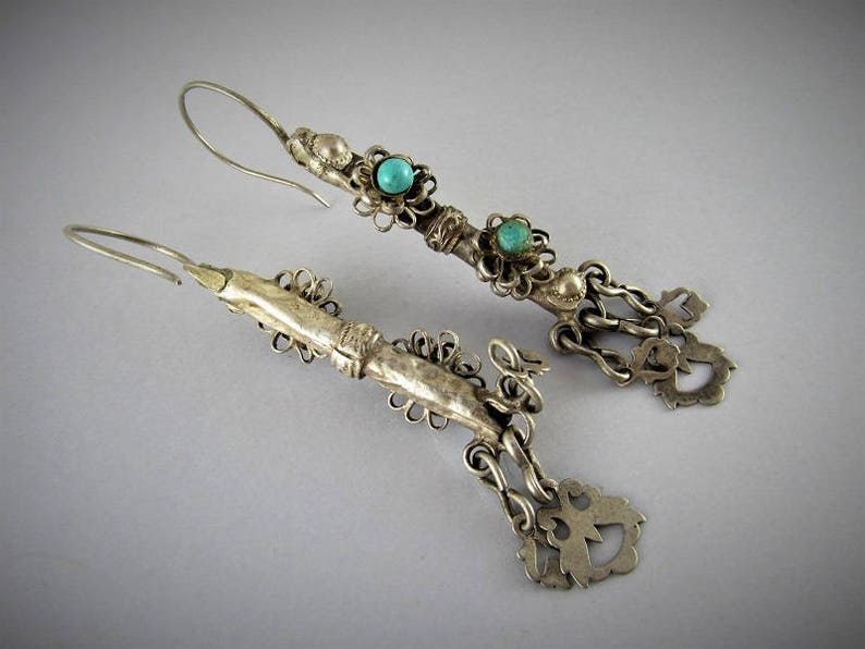 May include: A pair of silver earrings with turquoise stones and intricate filigree designs. The earrings are dangling and have a hook closure.