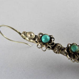May include: Silver dangle earrings with turquoise stones set in floral designs. The earrings have a hook closure.