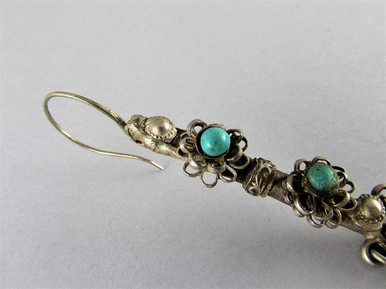 May include: Silver dangle earrings with turquoise stones set in floral designs. The earrings have a hook closure.
