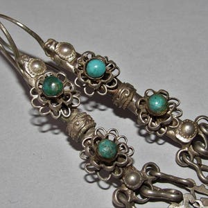 May include: A pair of silver earrings with turquoise stones and intricate floral designs. The earrings have a dangling chain with additional floral accents.