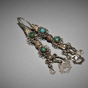 May include: A pair of silver earrings with turquoise stones and decorative filigree. The earrings have a dangling design with multiple charms.