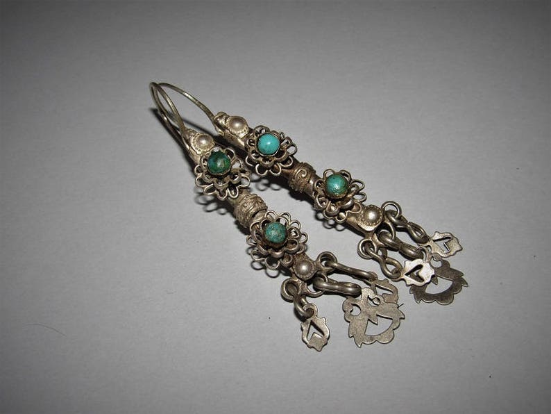 May include: A pair of silver earrings with turquoise stones and decorative filigree. The earrings have a dangling design with multiple charms.