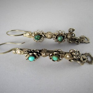 May include: A pair of silver earrings with turquoise stones and floral designs. The earrings are made of silver and have a dangling design.