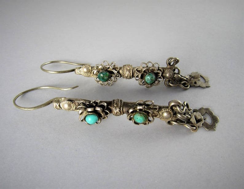 May include: A pair of silver earrings with turquoise stones and floral designs. The earrings are made of silver and have a dangling design.