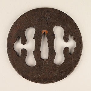 Op de afbeelding: Een ronde, ijzeren tsuba, een decoratieve bescherming voor een Japans zwaard, met een uitgesneden ontwerp van een gestileerde bloem.