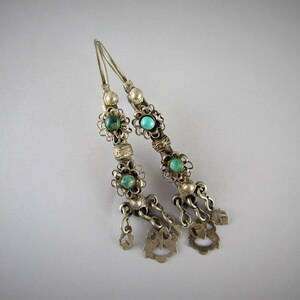 May include: A pair of silver earrings with turquoise stones and intricate filigree designs. The earrings have a dangling charm at the bottom.