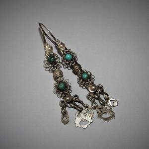 May include: A pair of silver dangle earrings with turquoise stones and intricate floral designs. The earrings have multiple small charms hanging from the bottom.