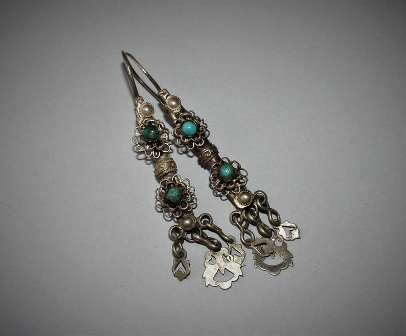 May include: A pair of silver dangle earrings with turquoise stones and intricate floral designs. The earrings have multiple small charms hanging from the bottom.