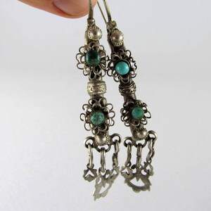 May include: A pair of silver earrings with turquoise stones and intricate filigree designs. The earrings have a dangling charm at the bottom.