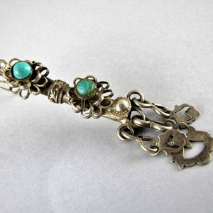 May include: A silver pendant with turquoise stones and intricate filigree details. The pendant features a chain with multiple decorative elements.