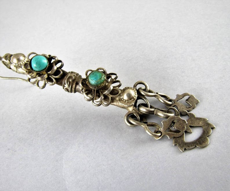 May include: A silver pendant with turquoise stones and intricate filigree details. The pendant features a chain with multiple decorative elements.