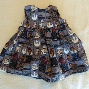 May include: A gray sleeveless dress with a Star Wars print featuring characters and the Millennium Falcon. The dress has a black background with white and red accents.