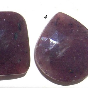 May include: Four purple gemstone cabochons with faceted surfaces. The cabochons are in various shapes, including oval, square, and teardrop.