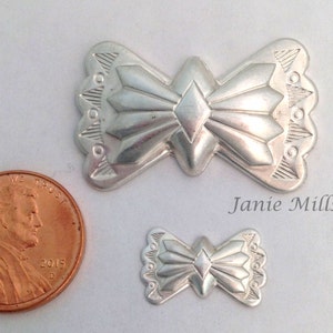 May include: Two silver metal pendants in the shape of a stylized bow with a diamond in the center. The larger pendant is about the size of a US penny.