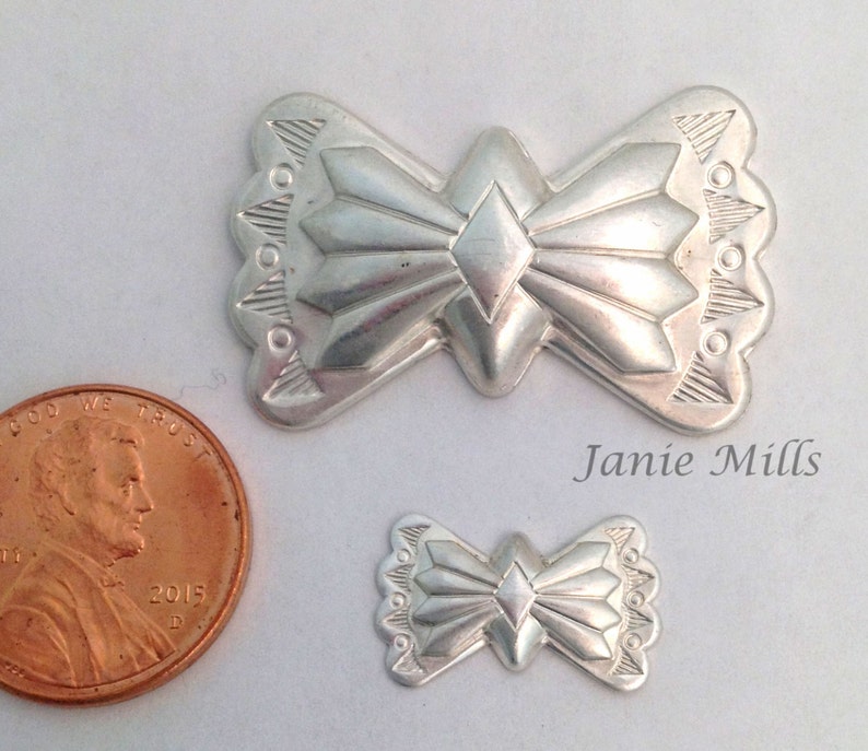 May include: Two silver metal pendants in the shape of a stylized bow with a diamond in the center. The larger pendant is about the size of a US penny.