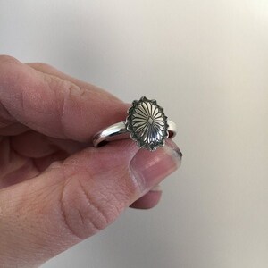 May include: A silver ring with a detailed, oval-shaped design. The design features a central starburst with radiating lines.