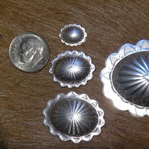 May include: Four silver oval-shaped conchos with a sunburst design. The conchos are different sizes, with the largest measuring 4.34 inches by 4.44 inches. The text "Oval sizes available in seperate listings" is visible in the image. 1) 10x13mm 2) 17x21mm 3) 23x29mm 4.34x44mm