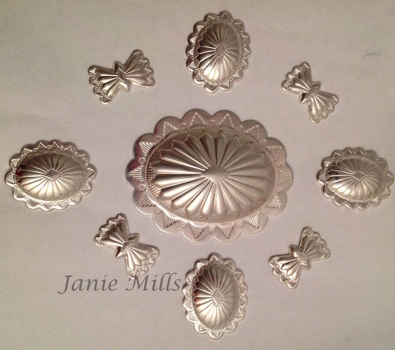 May include: Eight silver-toned metal embellishments with a sunburst design. The embellishments are in various shapes and sizes, including oval, round, and bow-shaped.
