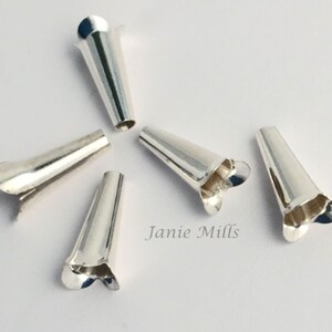 May include: Six silver cone-shaped jewellery findings with a flared, petal-like edge. The findings are arranged on a white surface. The text "Janie Mills" is visible in the lower right corner.