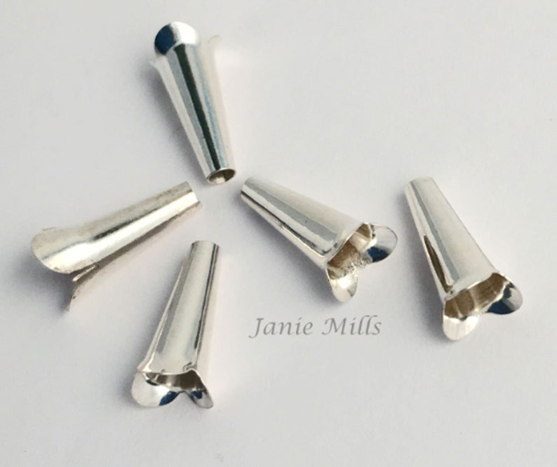 May include: Six silver cone-shaped jewellery findings with a flared, petal-like edge. The findings are arranged on a white surface. The text "Janie Mills" is visible in the lower right corner.