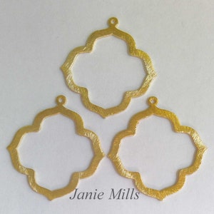 Puede incluir: Tres colgantes de metal dorado con un diseño de trébol de cuatro hojas. Cada colgante tiene un pequeño bucle en la parte superior para sujetarlo a un collar o pulsera.