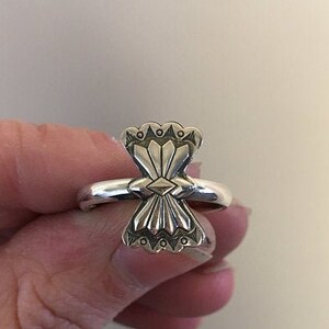 May include: A silver ring with a geometric design. The ring is worn on a finger.