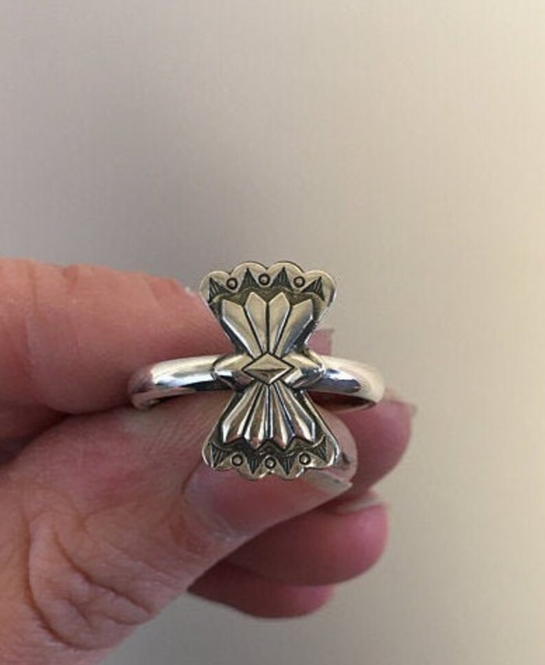 May include: A silver ring with a geometric design. The ring is worn on a finger.