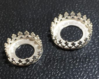 May include: Two silver crown-shaped metal settings with a round opening in the center. The settings are on a black surface.