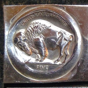 May include: A silver-colored metal coin with a raised image of a buffalo and the words "United States of America" and "Five" around the edge.
