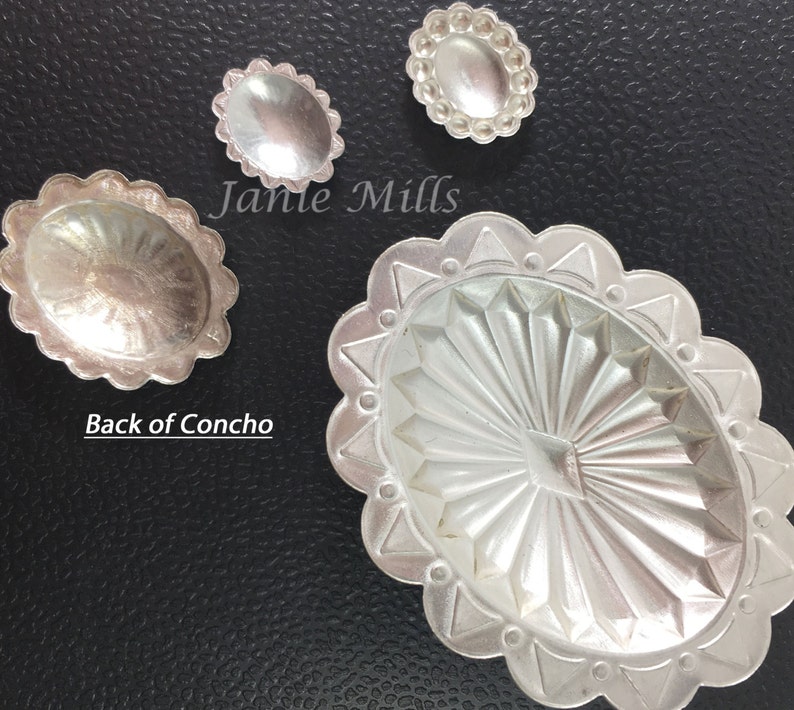 May include: Three silver concho shells with different designs. The largest shell has a sunburst pattern, the medium shell has a smooth surface, and the smallest shell has a beaded edge.