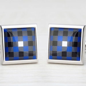 Op de afbeelding: Een paar zilveren manchetknopen met een zwart-blauw geruit patroon.
