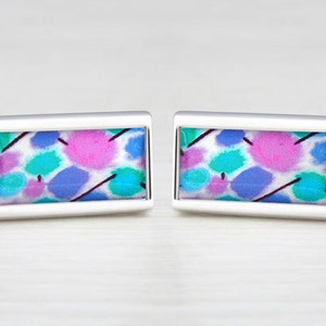 Peut inclure: Une paire de boutons de manchette en argent avec un design rectangulaire. Les boutons de manchette présentent un motif abstrait coloré avec des nuances de rose, de bleu et de vert sur un fond blanc.